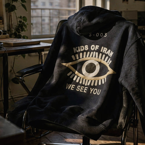 S-003 Open Eye hoodie back with S-003 code, eye graphic, and WE SEE YOU text, displayed on an office chair – Kids Of Iran