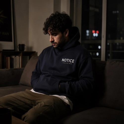 S-003 Open Eye hoodie with NOTICE and Kids Of Iran chest print, worn indoors at night
